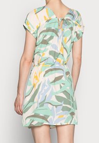Lyhythihainen mekko, jossa on lehdesign mintunvihreänä, beigenä ja keltaisena. Ominaisuuksiin kuuluu avaus takana ja kiristetty vyötärö, joka luo rennon istuvuuden.