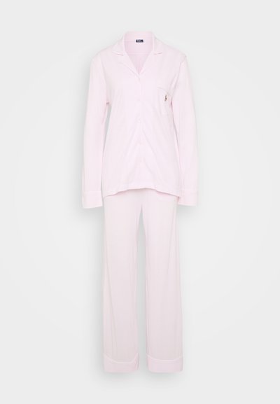 Ροζ πιτζάμα από μαλακό ύφασμα. Μπλούζα με μακριά μανίκια, πουκάμισο με λοξό γιακά και μικρή τσέπη στο στήθος. Ιδανικά ίσια παντελόνια.