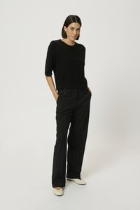 Top căptușit negru cu mâneci scurte umflate, asortat cu pantaloni negri cu dungi verticale, cu talie înaltă. Modelul poartă pantofi bej, având mâinile în buzunare.