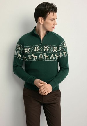 Zielony sweter dziany z kołnierzem na zamek. Na wysokości klatki piersiowej wzór jasnych reniferów i drzew. Ściągacze przy mankietach i u dołu.