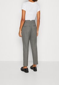 Pantalon à motif pied-de-poule gris, taille haute, avec deux poches arrière et coupe fuselée, associé à des chaussures noires.