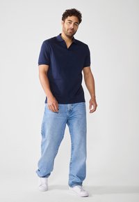 Marineblå ribbestrikket polo med splittet krage, parret med lyseblå, løstsittende jeans og hvite sneakers. Enkelt og uformelt design.