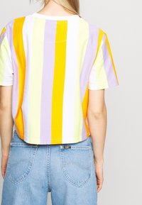 Lyhythihainen crop-top, jossa on oransseja, keltaisia, laventelin värisiä ja valkoisia pystysuoria raitoja, yhdistettynä vaaleansinihin farkkushortseihin. Puuvillakangasta.