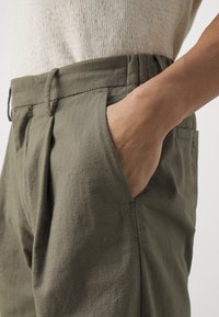 Pantaloni kaki in tessuto testurizzato, con una vestibilità comoda, pinces frontali e tasche laterali. La vita si adagia comodamente sui fianchi.