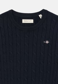 Maglione a collo rotondo di colore blu navy, lavorato a maglia con motivo a treccia e con un piccolo logo ricamato sul petto. Realizzato in un tessuto morbido e strutturato.