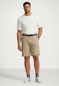 Bēša krāsas šorti ar jostu, balta īsām piedurknēm t-krekls ar nelielu logotipu, pelēkas zeķes un baltas sporta kurpes. Ikdienišķs apģērbs.