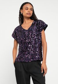 Lilla paliet-top med V-hals og korte ærmer. Stoffet har en skinnende, struktureret overflade med en løs pasform og afslappet design.