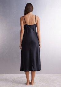 Vestido de satén negro, de longitud media, con tirantes finos y una textura suave, que presenta una vista trasera que destaca su diseño simple y ajuste.