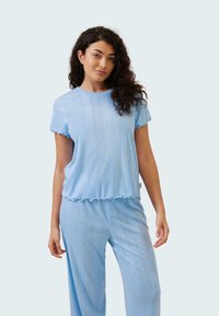 Ljusblå pyjamasset med en kortärmad topp med vågiga kanter och matchande byxor med en knappdetalj. Mjuk, texturerad väv.