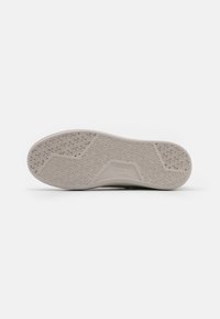 Semelle de chaussure présentant une forme incurvée, un matériau en caoutchouc gris texturé, et un motif de semelle détaillé pour améliorer l'adhérence et la traction.