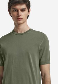 Olivgrön kortärmad t-shirt gjord av mjukt material, med rund halsringning och avslappnad passform, samt minimala sömnadsdetaljer.