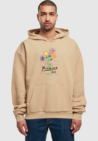 Felpa beige con tasca frontale e stampa grafica di fiori colorati con un design a mano. Realizzata in tessuto morbido, con polsini e orlo a costine.