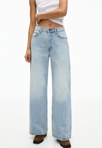 Hellblaue Schlagjeans aus Denim; mit hoher Taille, klassischem Fünf-Taschen-Design und leichtem Verblassen für Textur.
