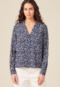 Blusa blu navy con motivo floreale in blu e bianco, caratterizzata da maniche lunghe, colletto a V e taglio morbido. Tessuto di texture liscia.