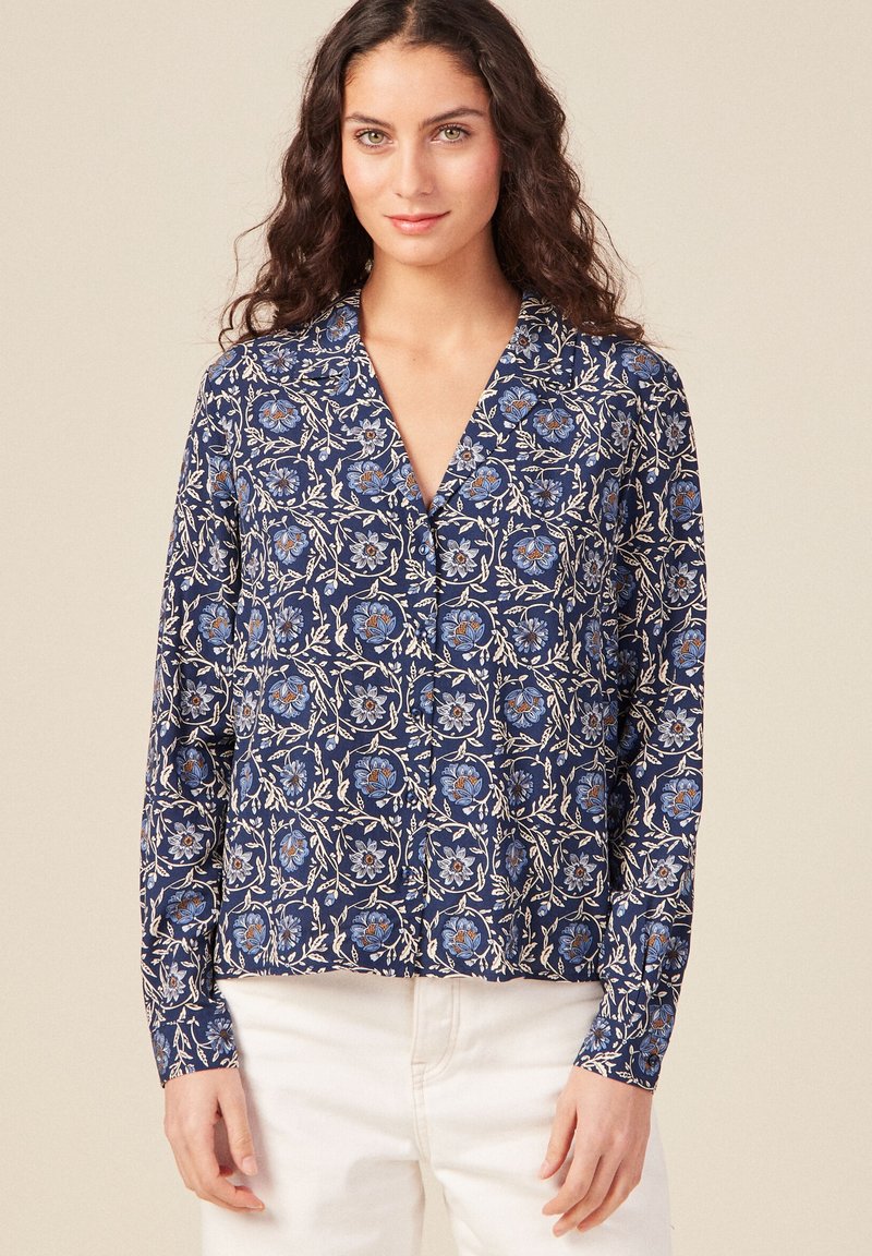 Blusa blu navy con motivo floreale in blu e bianco, caratterizzata da maniche lunghe, colletto a V e taglio morbido. Tessuto di texture liscia.