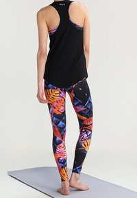 Black sleeveless tank top paired with colorful, patterned leggings featuring geometric shapes and leaf motifs in orange, pink, and blue tones.