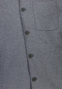 Grå knäppskjorta med en texturerad tyg, med sex svarta knappar framtill och en bröstficka på vänster sida.