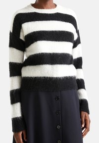 Černobílý pruhovaný svetr vyrobený z texturovaného, hebkého materiálu s kulatým výstřihem a dlouhými rukávy, v kombinaci s tmavou sukní na knoflíky vpředu.