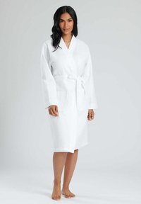 Accappatoio bianco da spa con tessuto texturizzato, maniche lunghe, cintura da annodare e due tasche frontali. Design di lunghezza intermedia, materiale morbido.