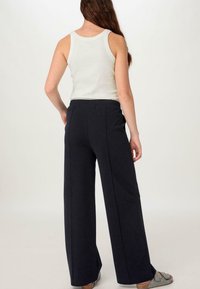 Zwarte wijde pantalon met een elastische tailleband, gemaakt van zachte stof, gecombineerd met een lichte tanktop. Model wordt van achteren getoond.