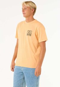 Korte mouwen, oranje katoenen T-shirt met een zwart logo op de linkerkant van de borst, ronde halslijn en een relaxed fit. Gekocht met blauwe denim shorts.
