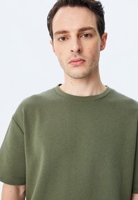 Oliven grøn bomuld t-shirt med korte ærmer og rund halsudskæring. Glat tekstur, enkelt design, ingen synlige mønstre eller accenter.