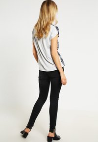 Grijze korte mouwen t-shirt met een bloemenontwerp aan de zijkant, gecombineerd met zwarte skinny jeans en zwarte enkellaarsjes met hak.