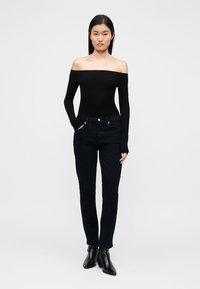 Schwarzer schulterfreier Body kombiniert mit dunklen Jeans. Die Jeans haben Vordertaschen und eine schlanke Passform, ergänzt durch Stiefeletten.