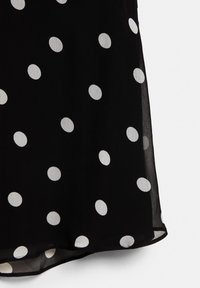 Fekete áttetsző anyag egyenletesen elhelyezkedő nagy fehér pöttyökkel, az alsó szegély egy enyhe ívét mutatva.