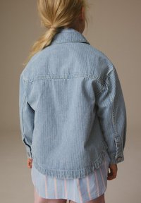 Randig denimjacka i ljusblått med avspänt snitt, långa ärmar, knappmanchetter och rundad nederkant. Bärs över en ljusblå randig skjorta.
