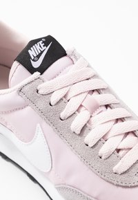 Rosa och grå sneaker med överdel i mocka och nylon, med en vit logotyp, svart logotypetikett och texturerade snören. Vit mellansula och svart yttersula.