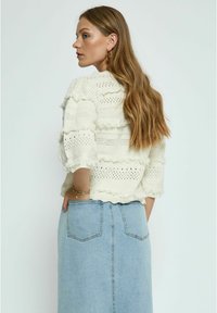 Haakgebreide trui in off-white met een gekruiste zoom en mouwen. Gecombineerd met een lichtblauwe denim rok met achterzakken.