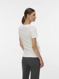 Άσπρο κοντομάνικο μπλουζάκι, εφαρμοστό σχέδιο, ομαλή υφή, στρογγυλή λαιμόκοψη, συνδυασμένο με σκούρο γκρι παντελόνι, ορατό από πίσω.