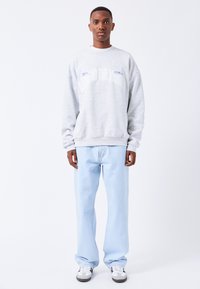 Sudadera de forro polar gris con texto blanco, combinada con vaqueros rectos de un azul claro y zapatillas grises y blancas. Conjunto simple y casual.