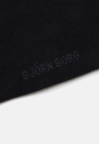 Materiale tessile nero con una superficie testurizzata, che presenta un logo appena visibile con la scritta "B.JÖRN BORG" in una stampa sottile e contrasta.