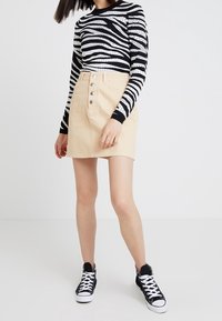 Maglietta a maniche lunghe a righe bianche e nere abbinata a una gonna di jeans beige chiaro con bottoni frontali e sneakers alte nere.
