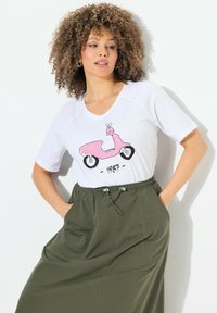 Camiseta blanca con gráfico de scooter rosa y el texto "1987", combinada con pantalones verdes de corte holgado con cintura ajustable.