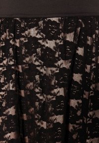 Svart spetskjol med elastisk midja, med blommönster och en semitransparent textur. Spetsen överlappar en solid bas.