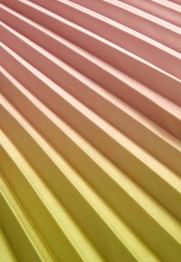 Gros plan sur des crêtes diagonales sur une surface avec un dégradé de couleurs allant du jaune au rose et une texture mate.