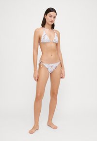 Twee-delige bikini met een bloemendessin, gemaakt van zachte stof. De top heeft driehoekige cups en verstelbare banden; de onderkant heeft zijkanten met strikjes.