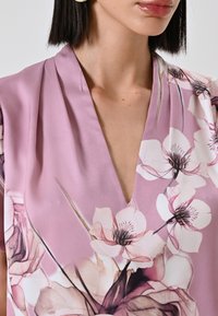Blusa floreale rosa con scollatura a V profonda, texture setosa, caratterizzata da grandi fiori in stile acquerello nelle tonalità di bianco e rosa pallido.
