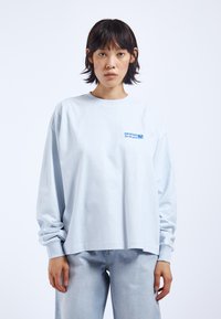 Helles blaues Langarm-T-Shirt aus Baumwolle, mit Rundhalsausschnitt und lockerer Passform. Kleines blaues Logo auf der linken Brustseite.