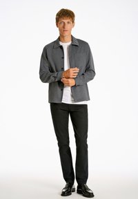 Grå button-up jacka över en vit skjorta, tillsammans med svarta byxor och skor. Har en krage och en bröstficka.