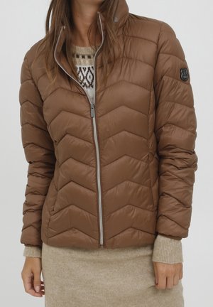 Veste marron matelassée avec fermeture éclair à l'avant portée sur un pull et une jupe beiges, montrant partiellement le haut du corps d'une personne.