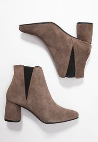 Bottines en suede marron avec un bout pointu, un talon épais et des panneaux latéraux élastiques pour un enfilage facile. Texture lisse avec des coutures minimales.