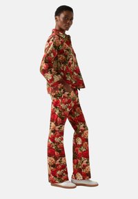 Floral print fabric outfit featuring a red and green color palette, with a relaxed-fit jacket and flared pants. White footwear completes the look.