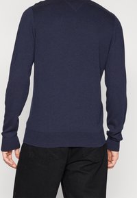 Pull-over bleu marine à manches longues avec ourlet côtelé. Fabriqué en matériau doux, il présente un col en V et une texture subtile.