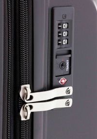 Cerniera di una valigia nera con due tiranti metallici, lucchetto approvato TSA e un combinatore numerico. Dettaglio della superficie testurizzata vicino all'area del lucchetto.