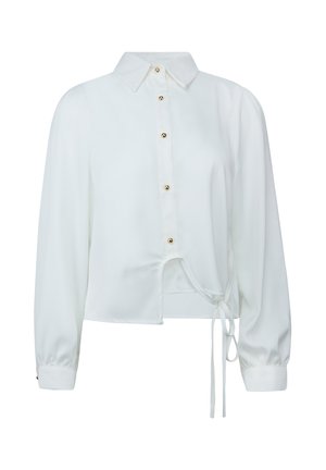 Blouse blanche à manches longues avec boutons dorés, col, poignets et un détail de nœud en bas devant.