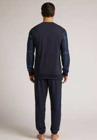 Marineblauw loungewear set: lange mouwen top met geruite mouwen en bijpassende joggers. Zachte stof, comfortabele pasvorm, ribgebreide manchetten en tailleband.